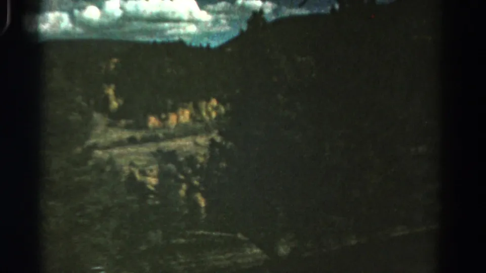 1967 Colorado 8mm frame showing a shadowed wooded roadside drop with cloudy sky and blurred terrain from a moving vehicle.