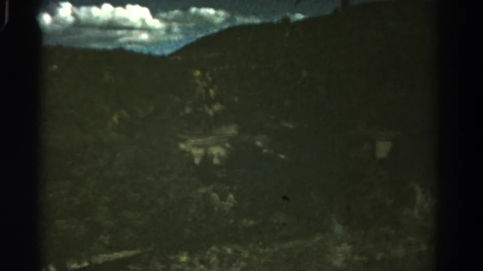1967 Colorado 8mm frame showing cloudy sky above a dark hillside and blurred roadside terrain from a moving car.