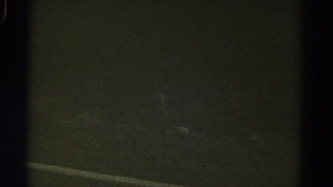 Dark road surface with a faint white lane marking seen from a moving vehicle.