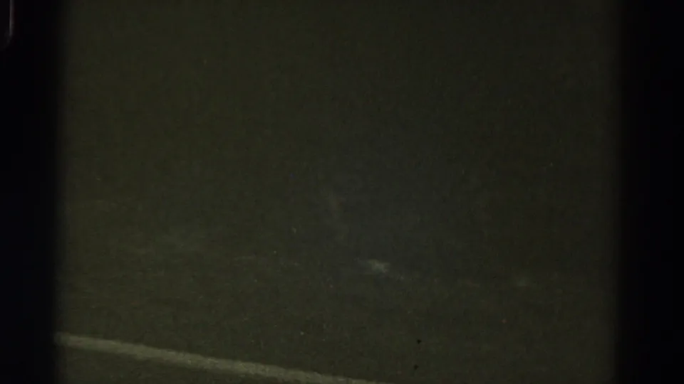 1967 Colorado 8mm frame showing dim pavement and a faint road marking during nighttime travel from a moving vehicle.