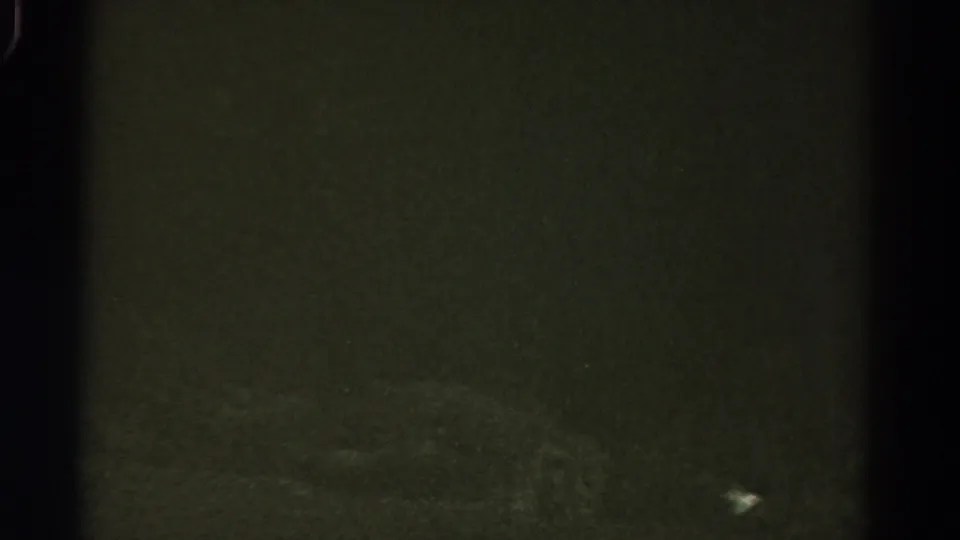 1967 Colorado night-driving frame with dim road texture, faint markings, and visible 8mm film grain.
