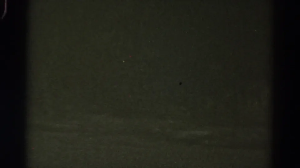 1967 Colorado 8mm frame showing an underexposed nighttime roadside view with dark vertical bars and indistinct green-black shapes.
