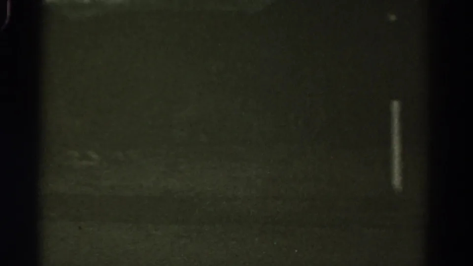 1967 Colorado 8mm night frame with a dark central band, murky roadside texture, and a narrow white light mark on the right.