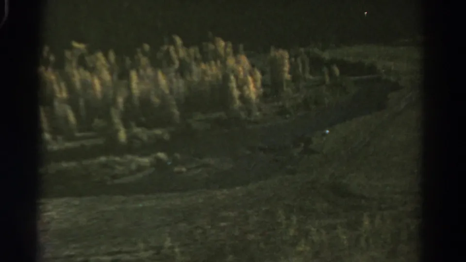 1967 Colorado home-movie frame with soft forested hills, a dark foreground slope, and a pale winding feature across the valley.