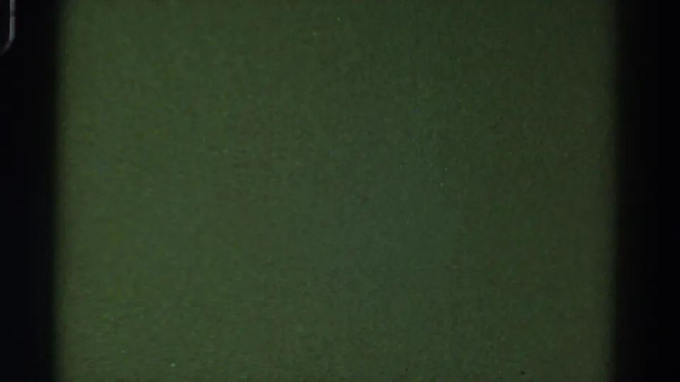 Blank green 8mm frame from the 1967 Colorado reel, with black vertical frame edge, visible grain, and scattered dust specks.