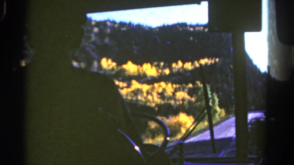 A passenger-view 8mm frame from Colorado in 1967 shows autumn forest through a bus windshield.