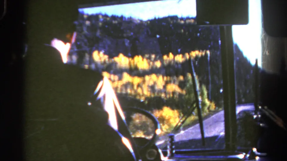 1967 Colorado home-movie view from inside a car, with a dark driver silhouette and golden autumn trees beyond the windshield.