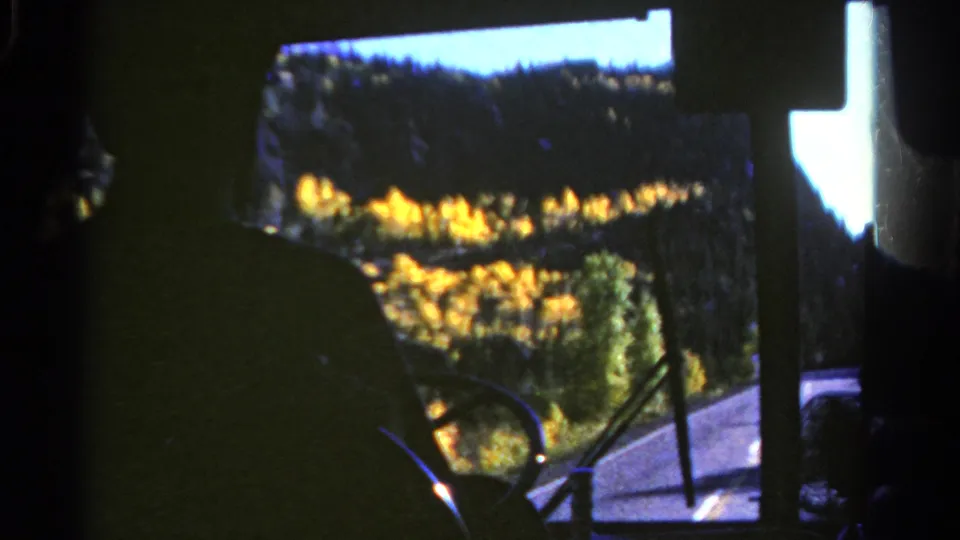 1967 Colorado driving footage from a dark vehicle interior, looking past the driver toward a road bordered by yellow autumn trees.