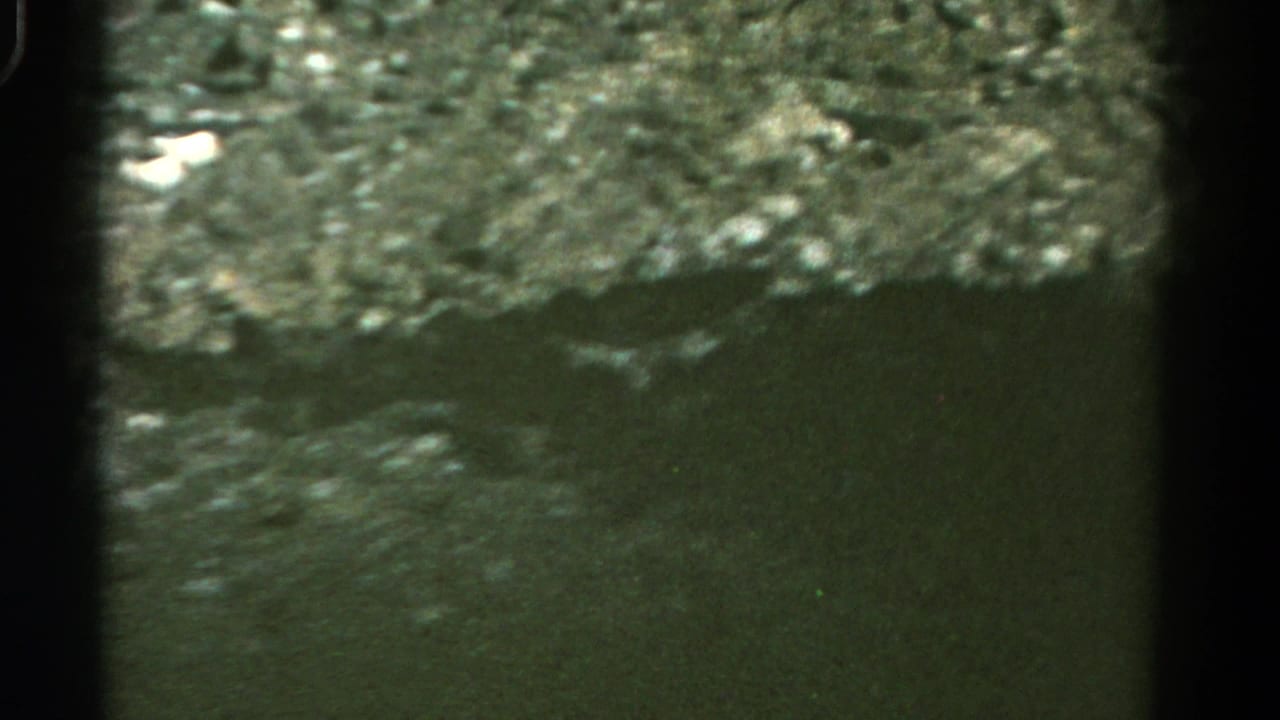 1967 Colorado home-movie frame showing a rocky hillside and shadowed roadside from a moving vehicle.