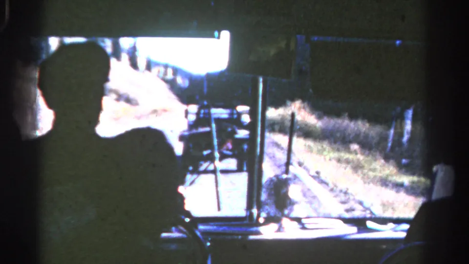 Silhouetted passenger inside a bus looks toward a truck ahead on a sunlit Colorado road in 1967 footage.