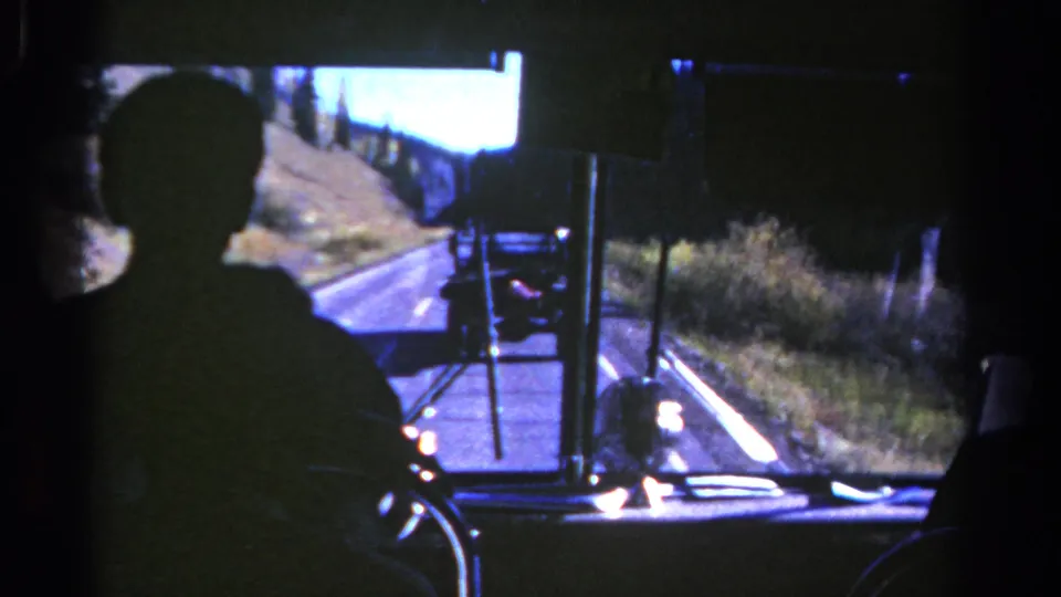 1967 Colorado bus-view frame with a silhouetted passenger, windshield framing, and a truck traveling ahead on a sunny rural road.