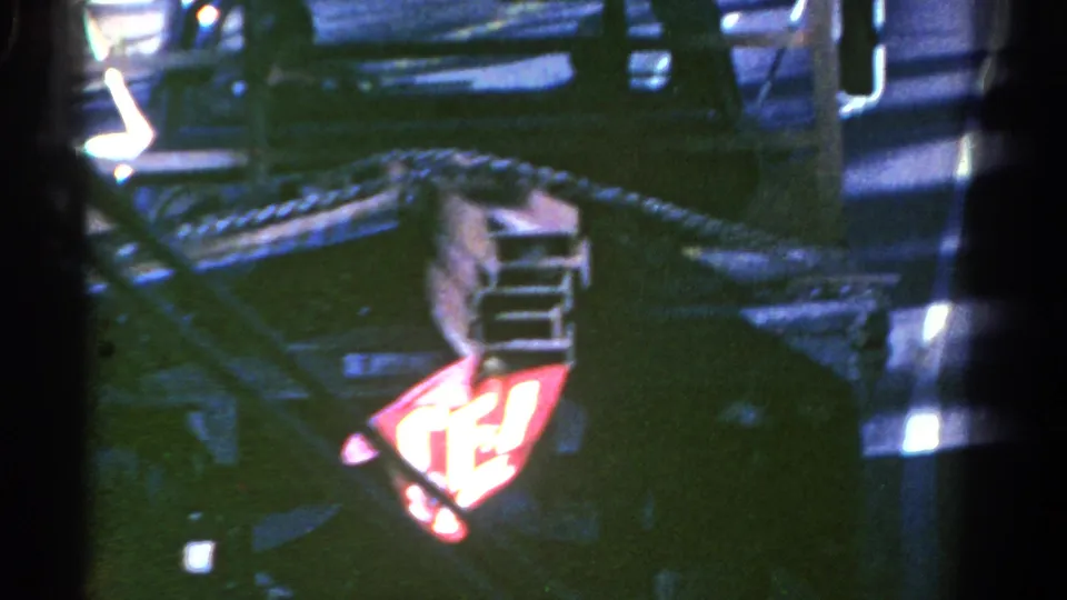 Interior 8mm frame from the Colorado bus journey, showing partial passengers, railings, windows, and a red illuminated sign or light.