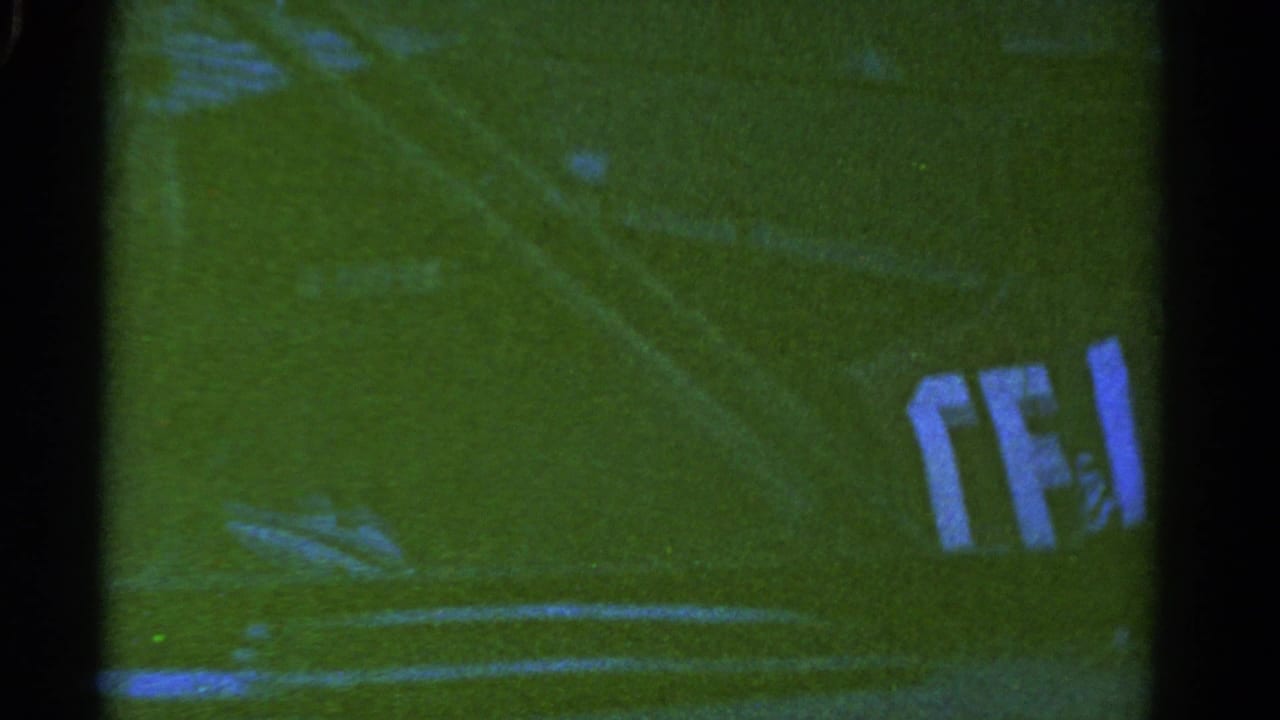 1967 Colorado 8mm frame showing a dark truck or trailer passing over a grassy field with white field lines and soft film blur.