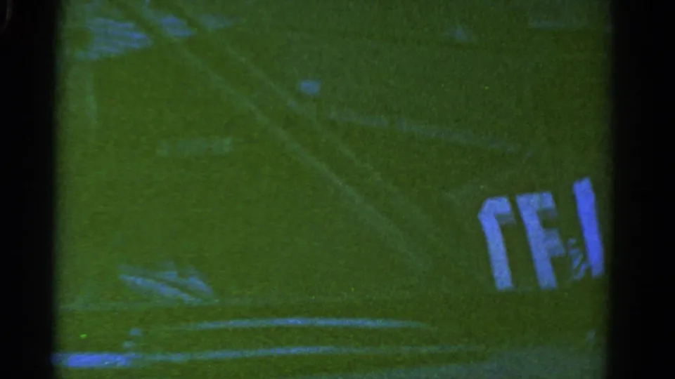 1967 Colorado 8mm frame showing a dark truck or trailer passing over a grassy field with white field lines and soft film blur.