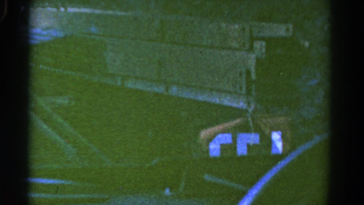 A dark truck or trailer side with visible lettering moves through a grassy Colorado field in this 1967 8mm frame.