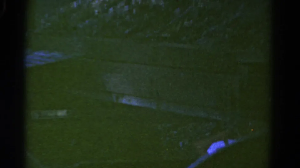 Soft 8mm frame from 1967 Colorado showing part of the moving truck or trailer against green grass and pale field markings.