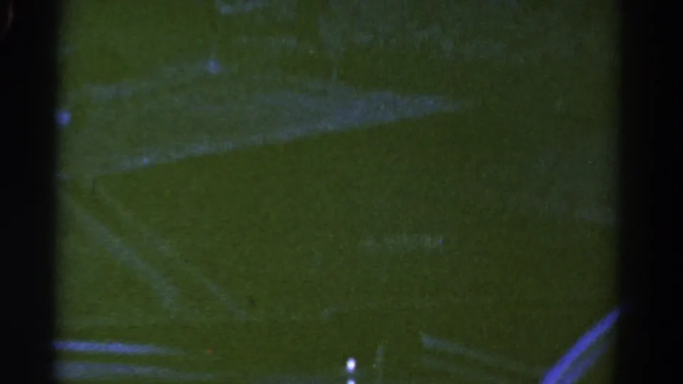 1967 Colorado home-movie frame looking through a dark car window at faint roadway markings and green-tinted roadside ground.