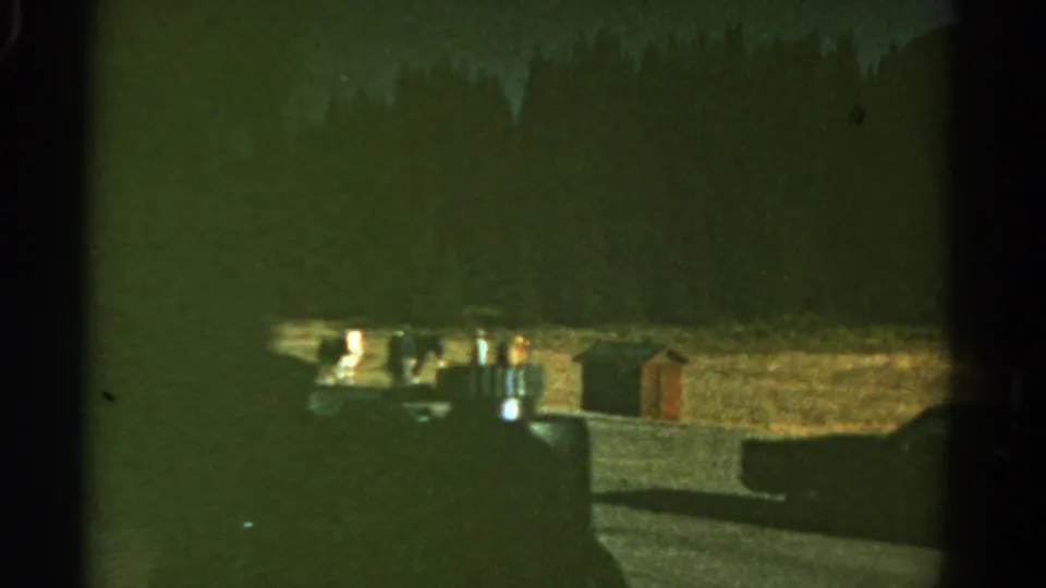 1967 Colorado home-movie frame showing a dim roadside stop with car-window framing, a parked vehicle shape, and small bright fixtures.