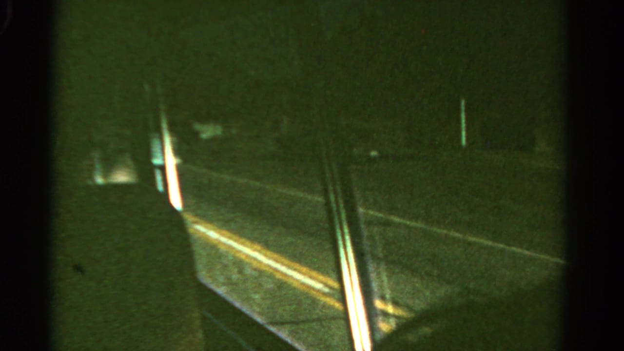 View from inside a vehicle looking past a window edge toward a dark road.