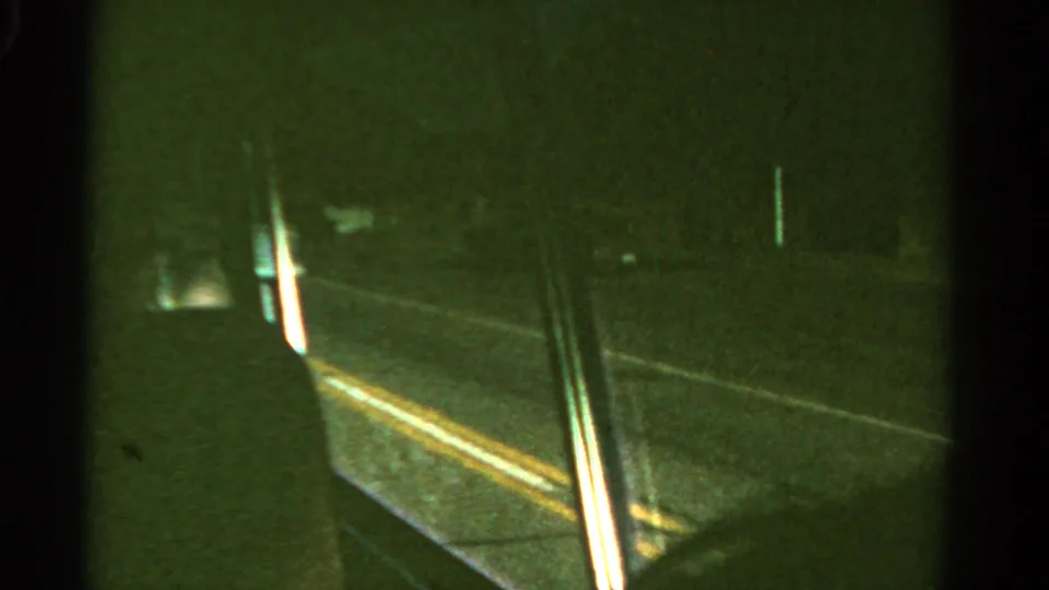 Passenger-side view from a moving vehicle in Colorado, with window framing, faint road lines, and darkness along a forested roadside.