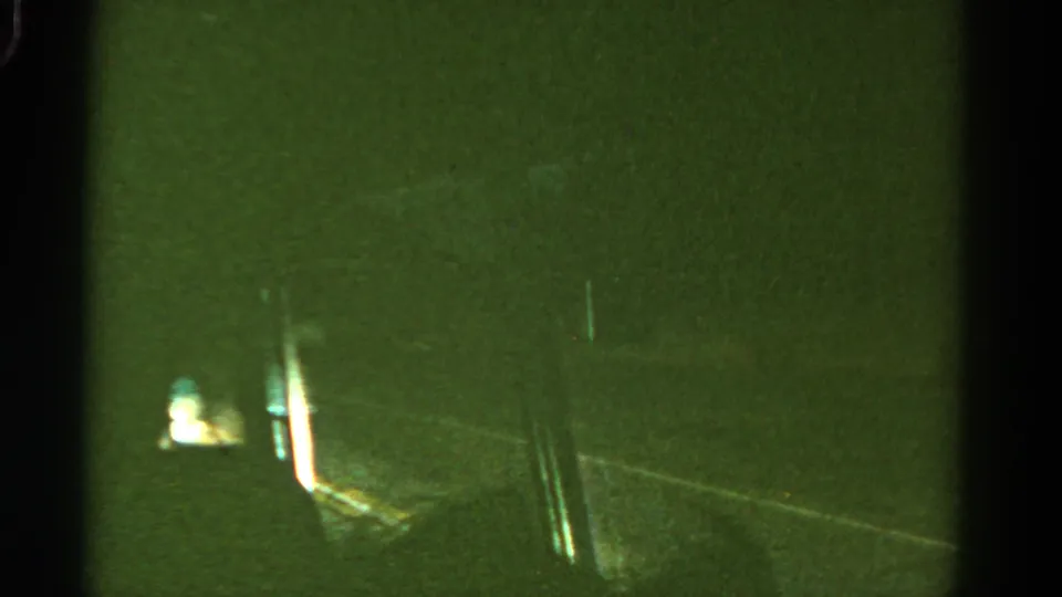 A dark Colorado road passes in a green-tinted 8mm frame, with small light flares and the vehicle viewpoint still apparent.