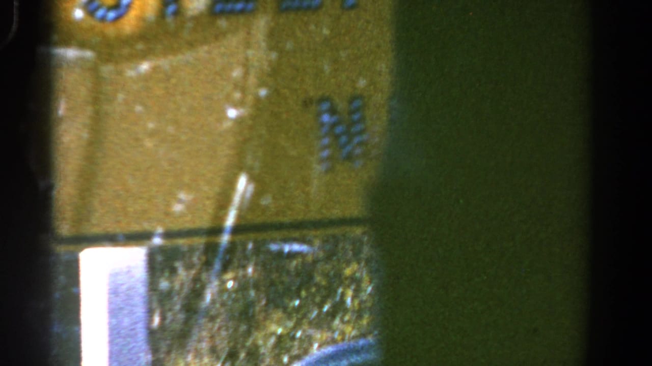 1967 Colorado 8mm frame showing part of a yellow roadside sign with blue lettering from inside a moving car.
