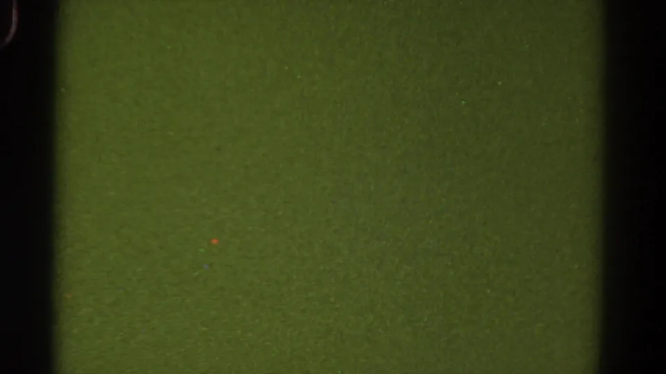 1967 Colorado 8mm home-movie frame showing a static green field with dark vertical borders, grain, and small speckles.