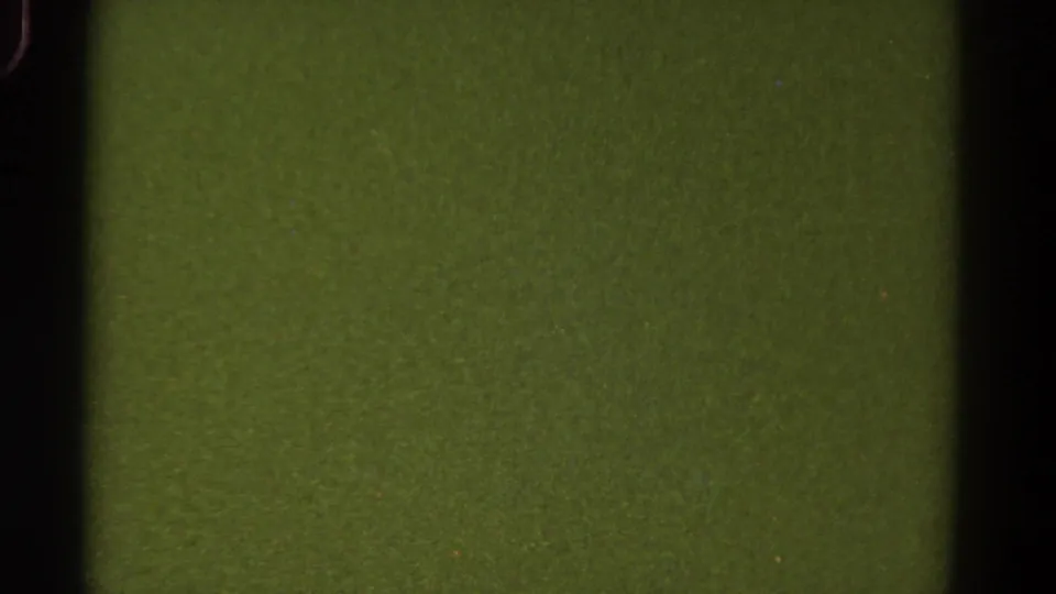 1967 Colorado 8mm still showing a blank green-tinted field with black frame edge, grain, dust specks, and subtle exposure variation.