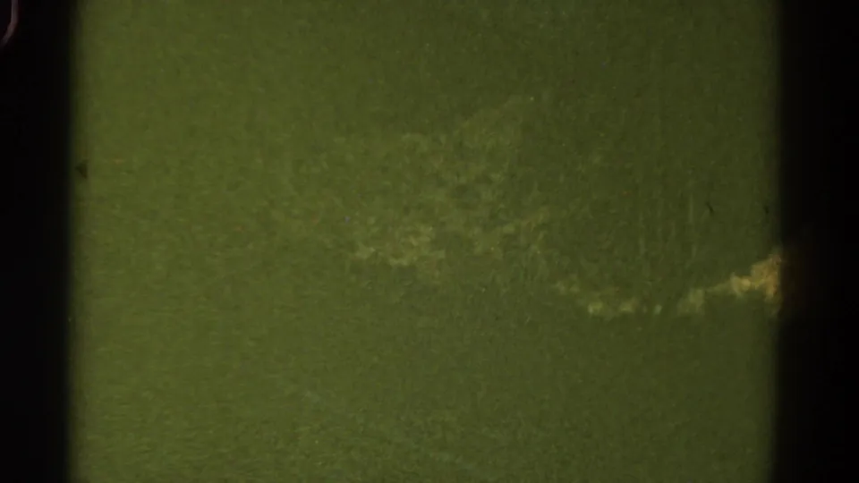 A green-tinted 8mm Colorado travel frame with indistinct terrain, gate shadows, scratches, and a pale moving highlight near the lower right.