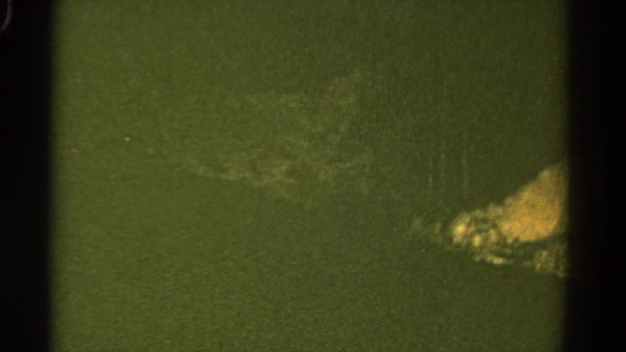 1967 Colorado 8mm travel frame showing a green slope and rocky roadside patch through soft, dark-edged film exposure.