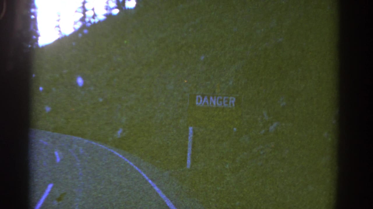 1967 Colorado 8mm frame showing a two-lane road curve, grassy embankment, trees, and a roadside DANGER sign.