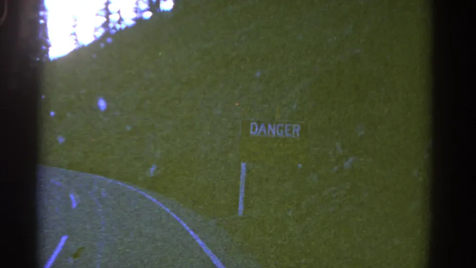1967 Colorado 8mm frame showing a two-lane road curve, grassy embankment, trees, and a roadside DANGER sign.