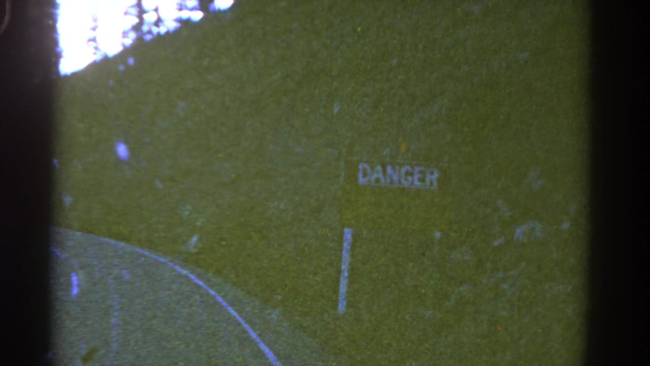 Road curve and hillside DANGER sign framed by dark film edges.