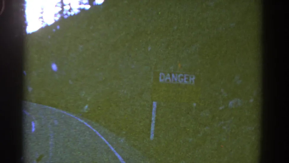 1967 Colorado 8mm view of a roadside DANGER sign on a green hillside above a curving two-lane road.