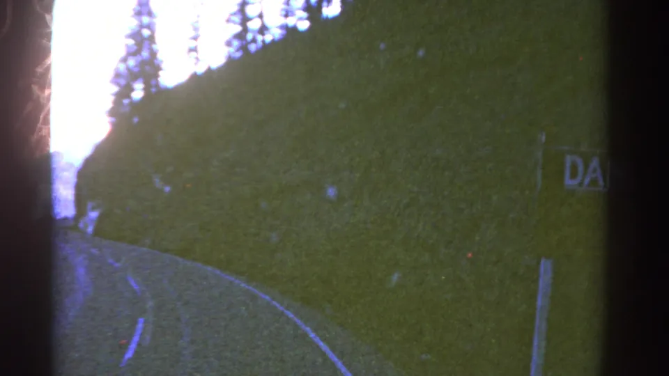 1967 Colorado 8mm frame showing the road curving forward while the hillside DANGER sign is partly cropped at the edge.