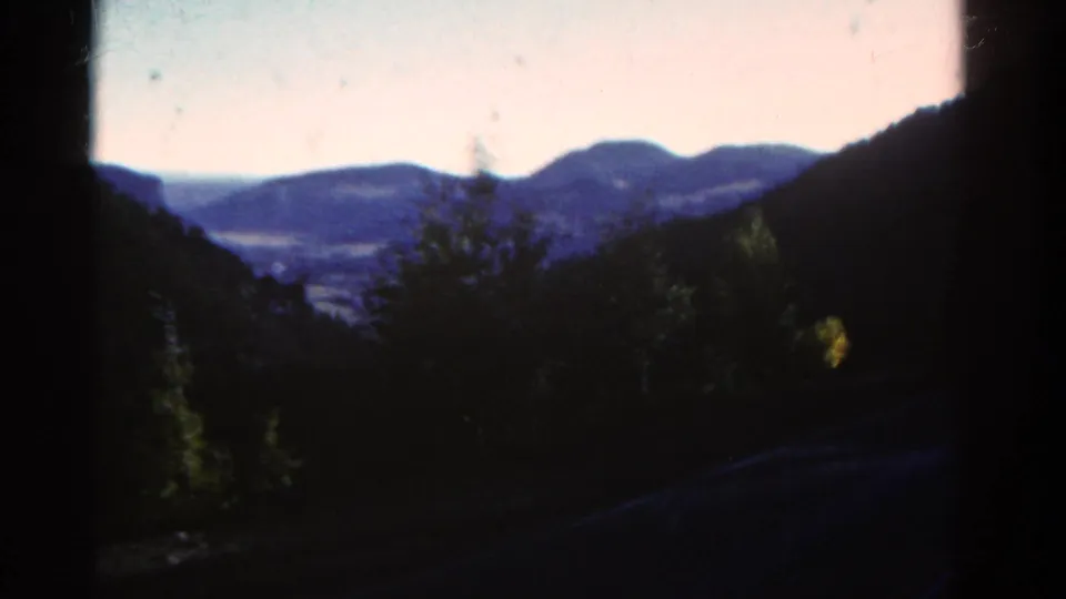 Soft 1967 Colorado 8mm view of mountain ridges beyond a dark, tree-lined valley.