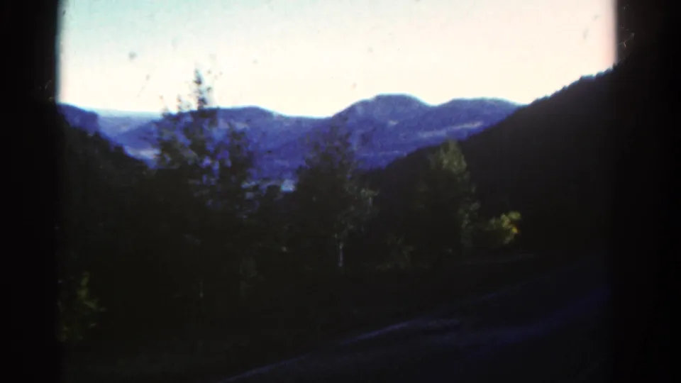 1967 Colorado 8mm frame with roadside trees, dark mountain slopes, and blue ridges in the distance.