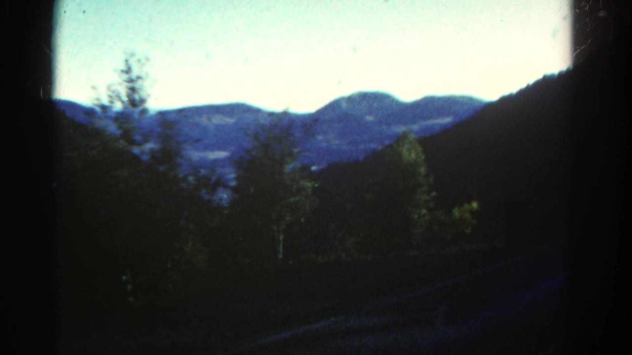 1967 Colorado home-movie view of blue mountain ridges, trees, and a valley seen through a dark window edge.