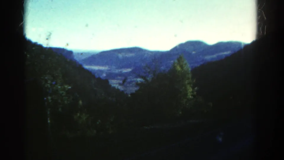 1967 Colorado mountain landscape with dark trees in the foreground and blue ridges visible through a vehicle window.