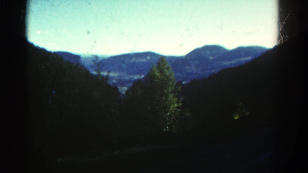 1967 Colorado 8mm frame showing a dark-edged view across foreground trees toward a valley and blue mountain ridges.