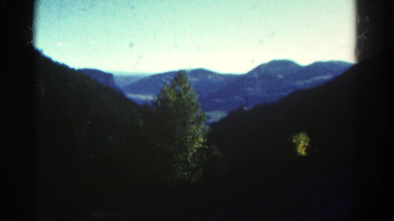 1967 Colorado 8mm frame with a central leafy tree, shadowed hillsides, distant ridges, and pale sky.