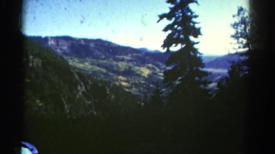 Colorado mountain landscape on 8mm film, with evergreen trees in shadow and rocky green hills beyond.