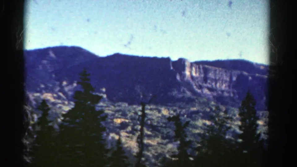 1967 Colorado scenic frame with a cliff band across the distance and evergreen silhouettes in the foreground.