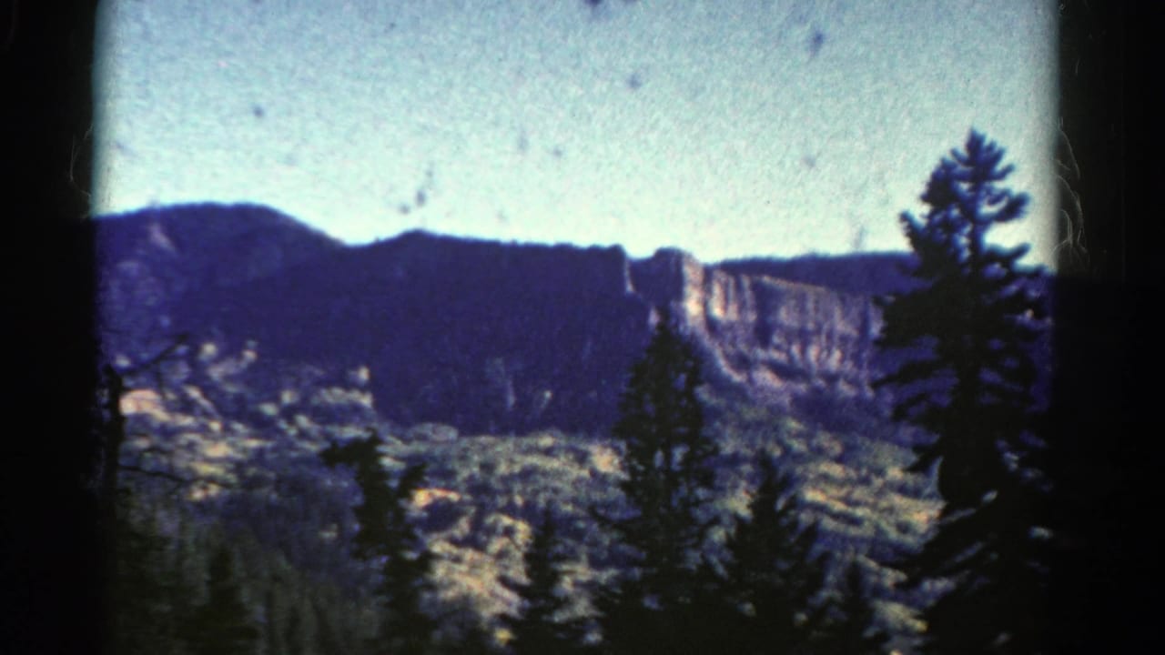 Distant cliff and mountain ridge seen beyond evergreen trees.