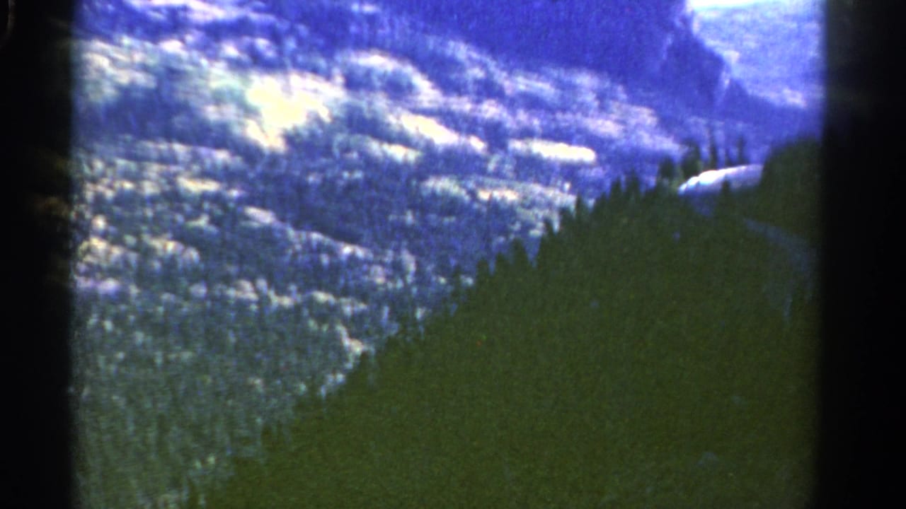 Colorado mountain scenery on 8mm film, showing a forested ridge below pale snow patches and distant rock forms.