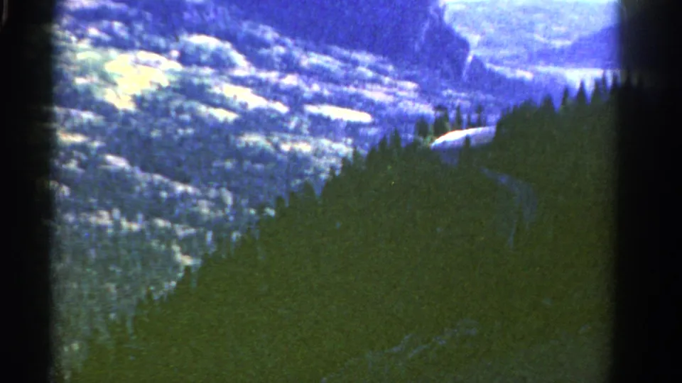 Colorado 8mm travel footage frame showing a winding road beneath evergreen slopes and snowy mountain scenery.