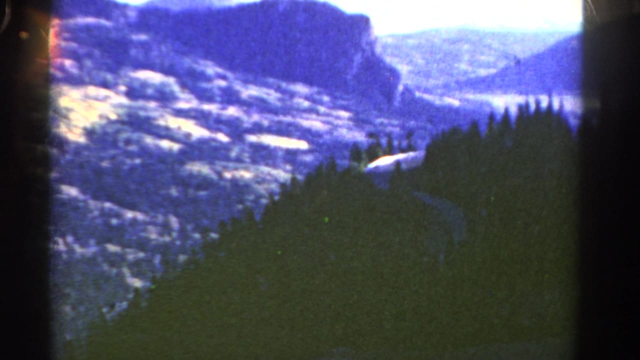 1967 Colorado 8mm frame showing a forested mountain valley, cliff walls, bright sky, and visible film-strip borders.
