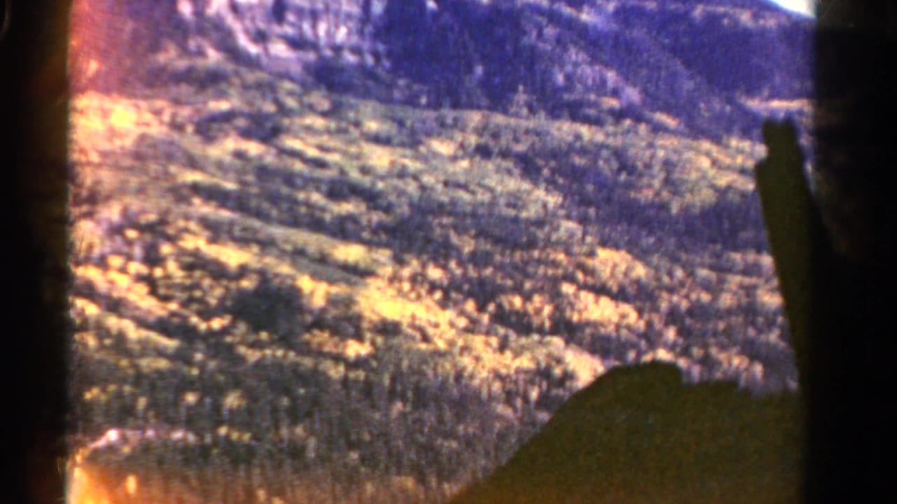 Soft, overexposed 1967 Colorado hillside view from inside a moving vehicle, with dark window framing in the foreground.