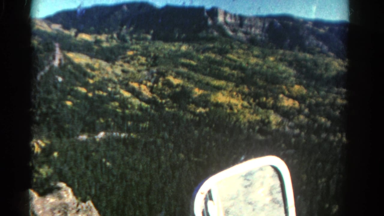 Wide mountain valley with a car mirror in the foreground and rocky ridges across the horizon.