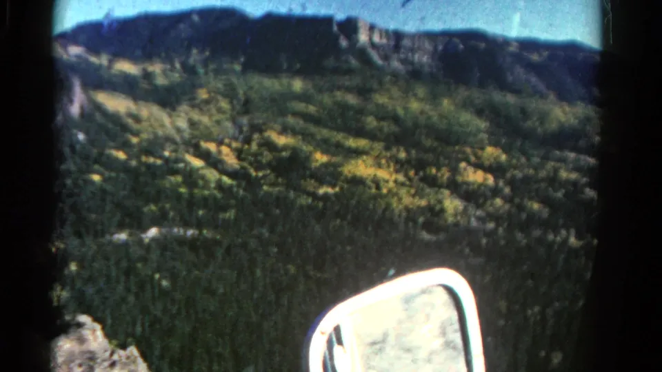1967 Colorado 8mm frame showing a soft, handheld view of a mountain valley with forest, yellow foliage, distant ridge, and car mirror.